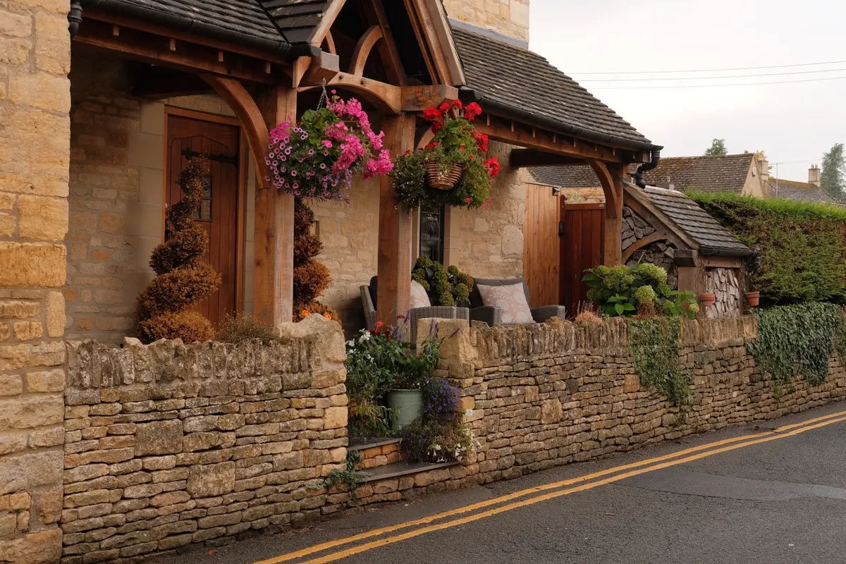 Cozy English cottage in the Cotswolds, adorned with vibrant hanging baskets and rustic stonework.